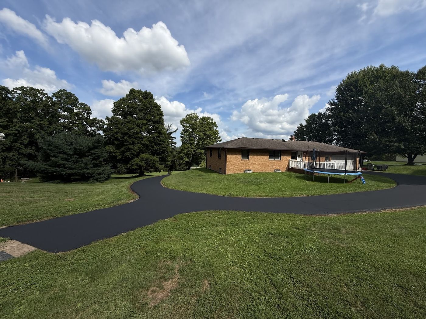 Long, freshly paved asphalt driveway winding across a lawn to a house